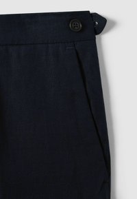 Pantaloni din in de culoare bleumarin închis, cu închidere cu nasture, pliseuri și buzunare laterale. Țesătura are un finisaj neted, cu textură.