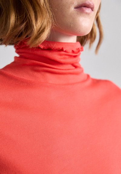 Ribbed turtleneck top in vibrant coral color with a frilled collar detail, featuring a soft texture and form-fitting design.