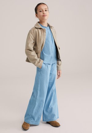 Gaisā zilas džinsa krekls ar pogām, bēša īsa jaka un platu kāju zili džinsi, kopā valkāti ar brūnām kurpēm. Vienkāršs dizains un vaļīgs piegriezums.