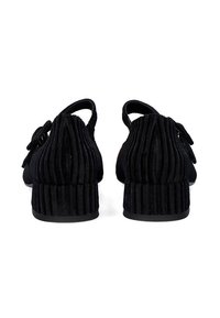 Zapatos negros texturizados con un diseño plisado, vista trasera, con un pequeño tacón y correa ajustable. El material parece suave y flexible.