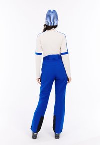 Blauwe skibroek met zwarte accenten, gecombineerd met een crèmekleurige longsleeve top met blauwe strepen. Een gebreide blauwe en witte beanie is gedragen.