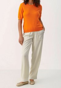 Helles orangefarbenes kurzärmliges Strickoberteil kombiniert mit hellbeigen, weit geschnittenen Hosen. Das Oberteil hat einen runden Ausschnitt, und die Hosen verfügen über Taschen vorne.