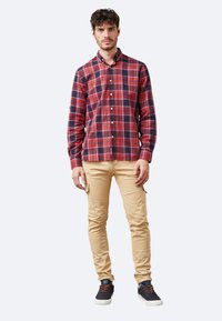 Camisa de cuadros roja y azul marino, de manga larga, fabricada en algodón. Combinada con pantalones cargo de color beige claro y zapatillas oscuras con detalles en naranja.