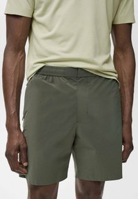 Shorts de sport vert olive avec un tissu lisse et léger. Comprend une taille élastique et des poches latérales pour plus de commodité.