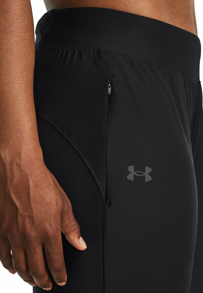 Pantaloni sportivi neri con una texture liscia e elastica, dotati di una tasca con zip sul lato e di un piccolo logo sulla coscia.