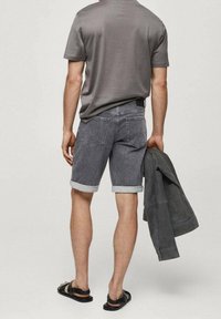 Szara koszulka, jasnoszare szorty z podwiniętymi nogawkami, czarne sandały, trzymając szarą kurtkę. Casualowy outfit o minimalistycznym designie.