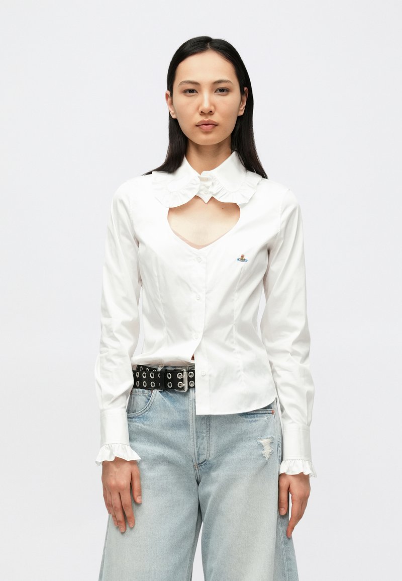 Vit skjorta med knappar fram, rynkad krage, hjärtformad utskärning framtill och broderad detalj. Matchad med ljusblå slitna jeans och svart skärp.