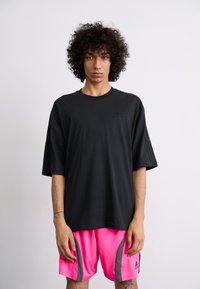 Sort oversized t-shirt med korte ærmer og rund hals. Har et subtilt logo på brystet. Sammen med livlige pink shorts med grå accenter.