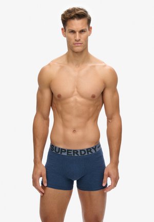 Boxers cortos para hombre en azul marino, hechos de una tela suave. Presentan una cinturilla elástica negra con la marca "SUPERDRY". Diseño simple y ajustado.