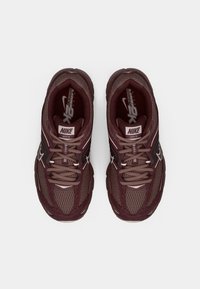 Zapatos Nike de color granate, con detalles de malla y superposiciones texturizadas. Cuentan con cordones, una suela acolchada y la marca reconocible en la lengüeta.