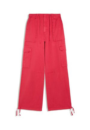 Pantalon cargo large rouge vif avec grandes poches avant et latérales, taille avec cordon et liens aux chevilles sur fond blanc.