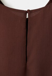 Tissu côtelé brun foncé avec une petite fermeture à bouton et boucle en haut, créant un détail d'ouverture en forme de trou de serrure.