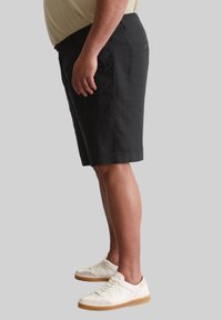Zwarte linnen shorts met zijzakken, rechte snit en een achterzak met knoop. Draag ze met witte sneakers met een rubberen zool.