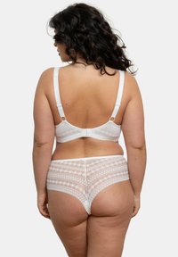 Ensemble de lingerie en dentelle blanche comprenant un bralette décoratif avec des bretelles ajustables et un slip taille haute transparent assorti. Motifs géométriques visibles.