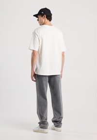 Camiseta de algodón blanca combinada con pantalones de mezclilla gris sueltos. Zapatillas blancas completan el conjunto. La camiseta tiene un corte relajado y mangas cortas.