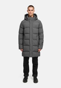 Sivý vyp padded kabát s vysokým golierom a kapucňou, so zapínaním na zips a bočnými vreckami, nosený cez čierne nohavice a topánky.