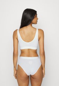 Λευκό βαμβα�κερό bralette με φαρδιές τιράντες και σχήμα σκαφτού στην πλάτη, συνδυασμένο με λευκές ψηλόμεσες βρακάκια που διαθέτουν κοψίματα σε σχήμα καρδιάς στο πίσω μέρος.
