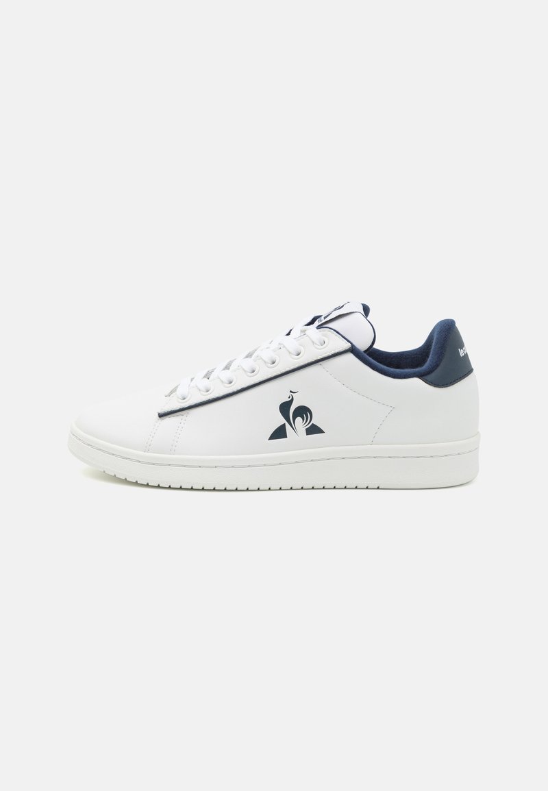 Baskets blanches avec une texture lisse, accents bleu marine, design à lacets, logo sur le côté et semelle plate en caoutchouc pour une meilleure adhérence.