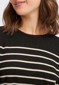 Maglione nero a maglia con strisce orizzontali bianche, caratterizzato da un collo rotondo e una texture sottile, mostrando una vista ravvicinata del tessuto.