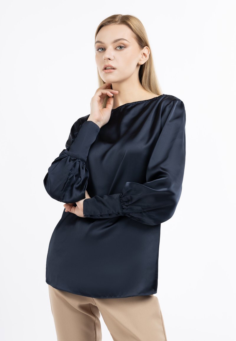 Blusa in satin blu navy con vestibilità rilassata, scollo rotondo e maniche a sbuffo voluminose. Texture liscia, rifinita con dettagli a bottone ai polsini.
