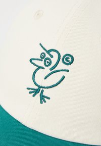 Casquette blanche avec un visière turquoise, ornée d'un design d'oiseau brodé. Le tissu est texturé, montrant des détails de couture à la surface.