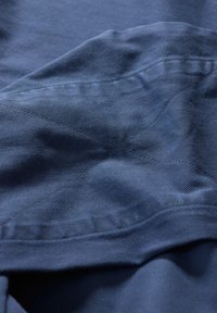 Mörkblått tyg med en texturerad yta; visar synliga sömmar och små veck, vilket framhäver en mjuk och draperad look.