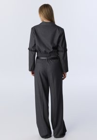 Grijze stoffen outfit met een getailleerde jas met een geraffineerde taille en wijde broekspijpen. Kenmerken zijn onder andere elastische manchetten en een ceintuuraccent.