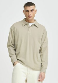 Lichtbeige poloshirt met lange mouwen, een klassieke kraag, een drie-knopen sluiting en geribbelde manchetten, gecombineerd met crèmekleurige broek.