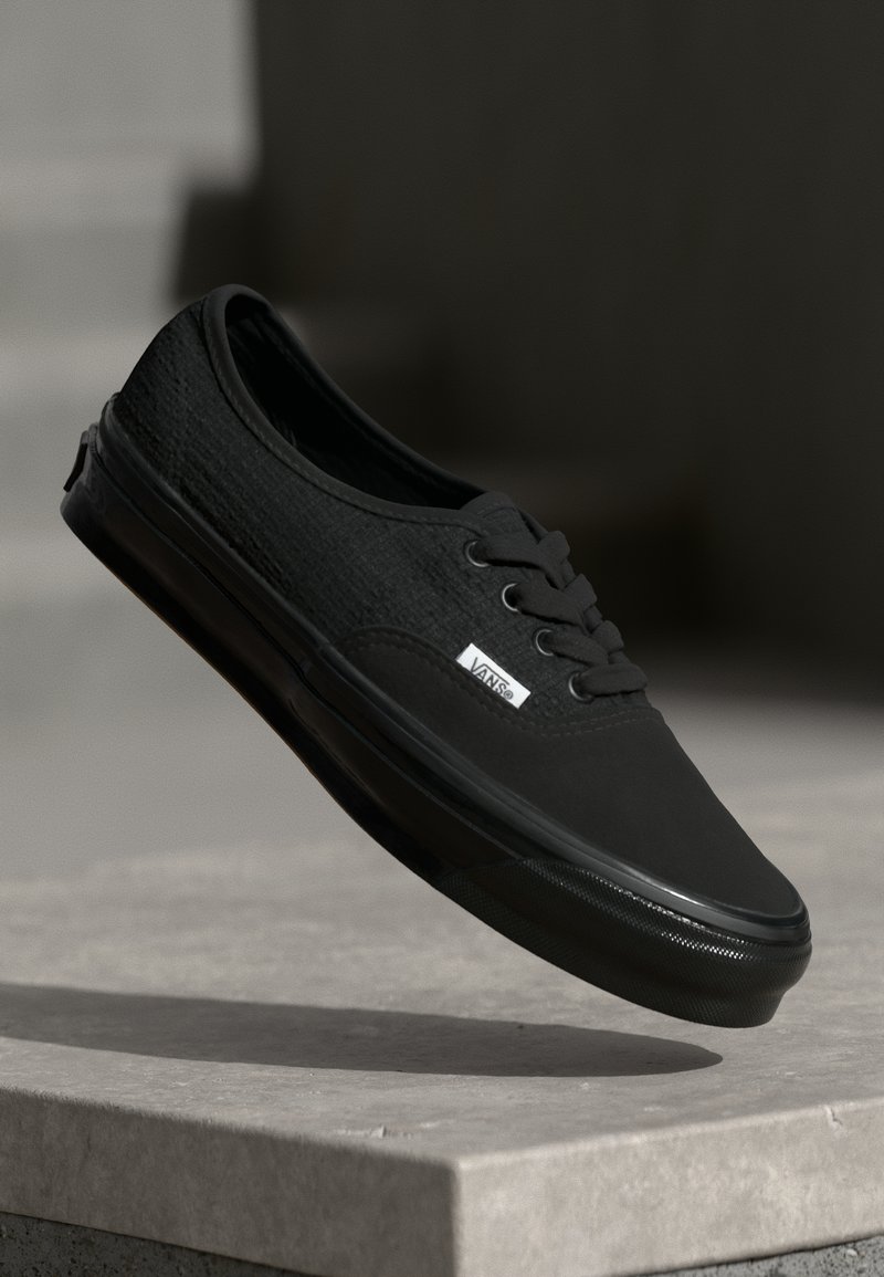 Schwarze Leinensneaker mit texturiertem Finish, runder Zehenpartie, Schnürdesign und einem Logo-Tag an der Seite. Verfügt über eine Gummisohle für guten Halt.