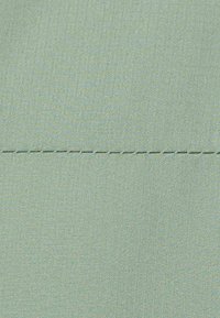 Tessuto verde chiaro con texture e motivo a griglia, caratterizzato da una cucitura visibile in filo chiaro che attraversa il centro.