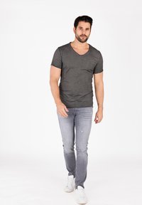 Camiseta gris de cuello en V con mangas cortas, combinada con jeans de mezclilla azul claro y zapatillas blancas. Leve textura y detalles desgastados en los jeans.