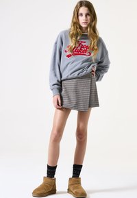 Sudadera gris con gráfico rojo, mini falda de pata de gallo, calcetas negras con patrón y botines marrones, exhibidos sobre un fondo blanco.