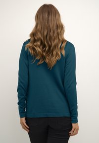 Tyrkysová dlouhá halenka vyrobená z měkké tkaniny. Má kulatý výstřih, slim fit a jednoduchý design lemování. Nosit s černými kalhotami.