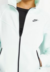 Light mint green Nike zip-up hoodie with black accents, featuring a front zipper, side pockets, and a hoodie with a soft fabric texture.