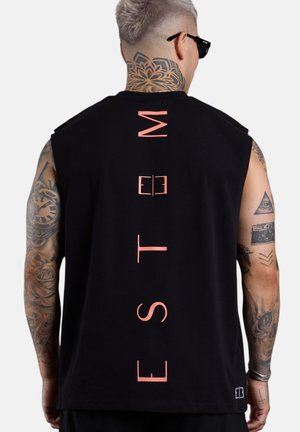 Mann mit Tattoos und Sonnenbrille, der ein schwarzes ärmelloses Oberteil mit vertikalem pinkem "ESTEN"-Schriftzug auf dem Rücken trägt.