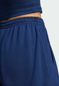 Närbild av en person som bär marinblå sweatpants med elastisk midja och en matchande ribbad topp, som visar sidofickans detalj.