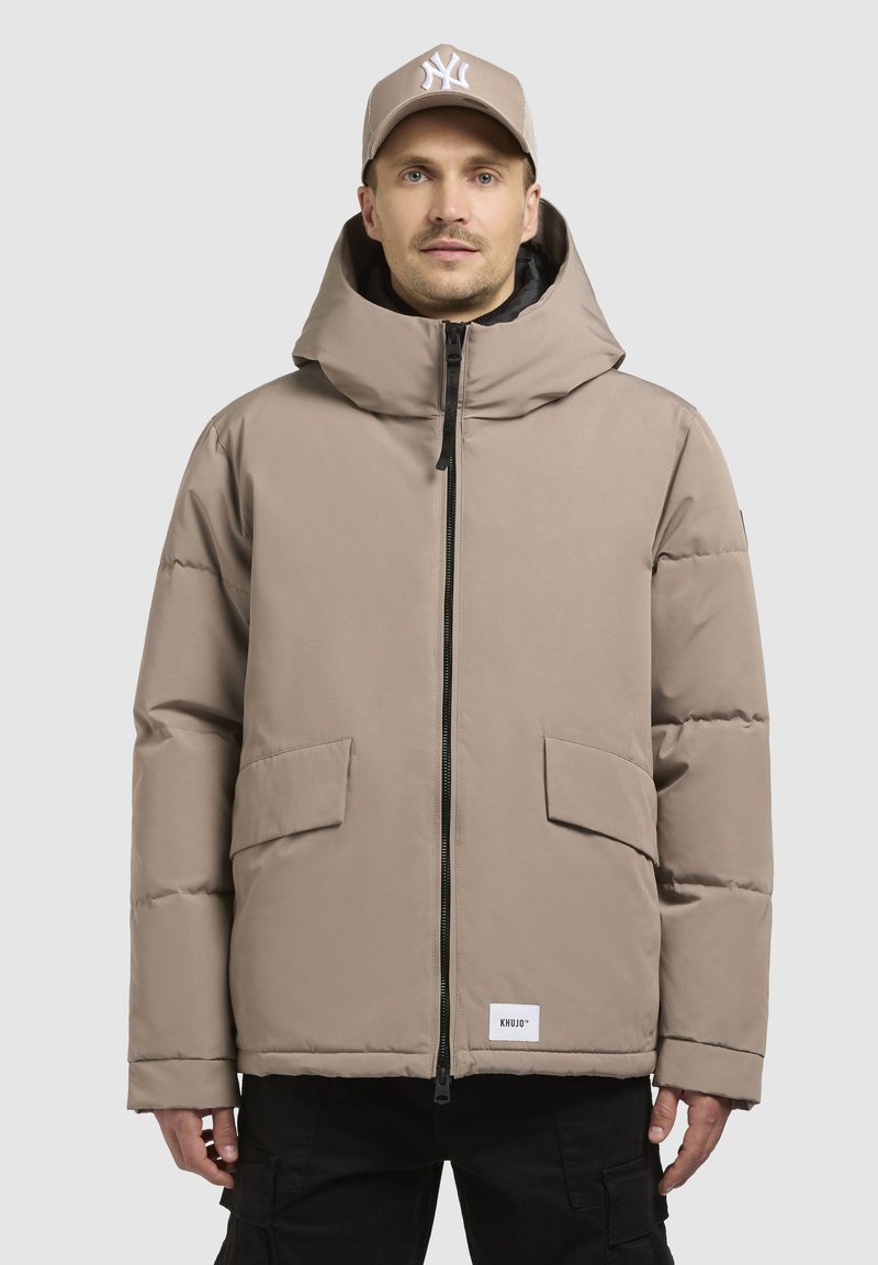 Bežna puffer jakna s visokim ovratnikom, prednjim zatvaračem i dvije velike džepove. Ima mekanu teksturu i uključuje oznaku s logotipom na rubu.
