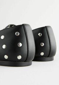 Le scarpe in ecopelle nera presentano una punta arrotondata e un tacco piatto, decorate con borchie argentate lungo la parte posteriore per un tocco di stile.