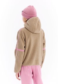 Beige fleecejack met capuchon, met roze accenten langs de mouwen. Gladde textuur, casual pasvorm. Draag met lichtroze broek.