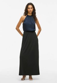 Top sans manches en satin marine avec un col froncé, associé à une jupe maxi fluide noire. Comprend des accents de talons métalliques à lanières.