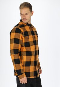 Ruteet flannelskjorte med orange og sorte farver, frontlommer, knaplukning og lange ærmer med klassisk kravedesign.