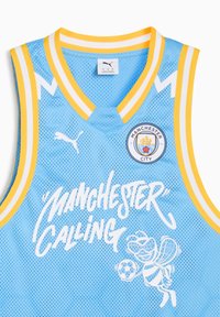 Világoskék kosárlabda mez sárga és fehér csíkos díszítéssel. A "Manchester Calling" felirat és egy méhecske grafika látható, amely focilabdát tart.