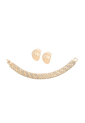 Goldfarbene, strukturierte Clip-Ohrringe und breites Armband mit geometrischem Muster und kleinen Perlenakzenten auf weißem Hintergrund.