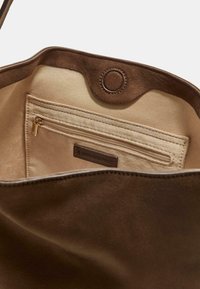 Interno di una borsa tote in suede marrone con una fodera beige liscia e una tasca con zip. Presenta un'etichetta del marchio e un dettaglio di chiusura a scatto.
