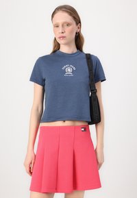 T-shirt bleu court avec un logo blanc et une jupe plissée rose avec un badge de marque sur la taille. Texture lisse, design décontracté.