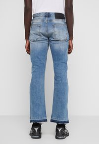 Vaqueros de mezclilla azul claro con diseño de pierna recta, con secciones descoloridas, dos bolsillos traseros y un dobladillo sin rematar en los tobillos.