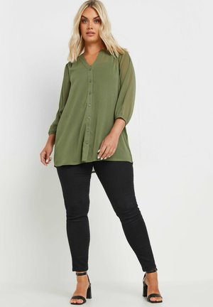 Green button-up blouse with a V-neck, sheer sleeves, and a loose fit, paired with black skinny jeans and black strappy heels.