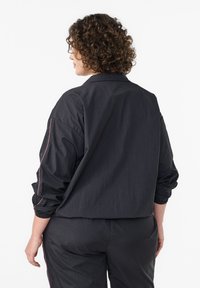 Melna viegla jaka ar elastīgām aprocēm, brīva piegriezuma un rozā akcenta diegu šuvēm. Bezšuvju dizains ar klasisku apkakli un minimālistisku stilu.