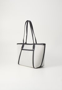 Sac fourre-tout en toile grise avec des finitions en cuir noir, deux anses longues et des détails de couture visibles sur les bords et les coutures.
