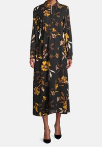 Långärmad klänning med krage i svart tyg med stor blommönster i gult, krämfärgat och brunt. Har en rynkad midja och är ankel-lång.